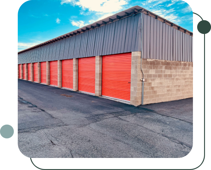 A long row of storage unit garages with red doors, a paved driveway in front, and a partly cloudy sky above.